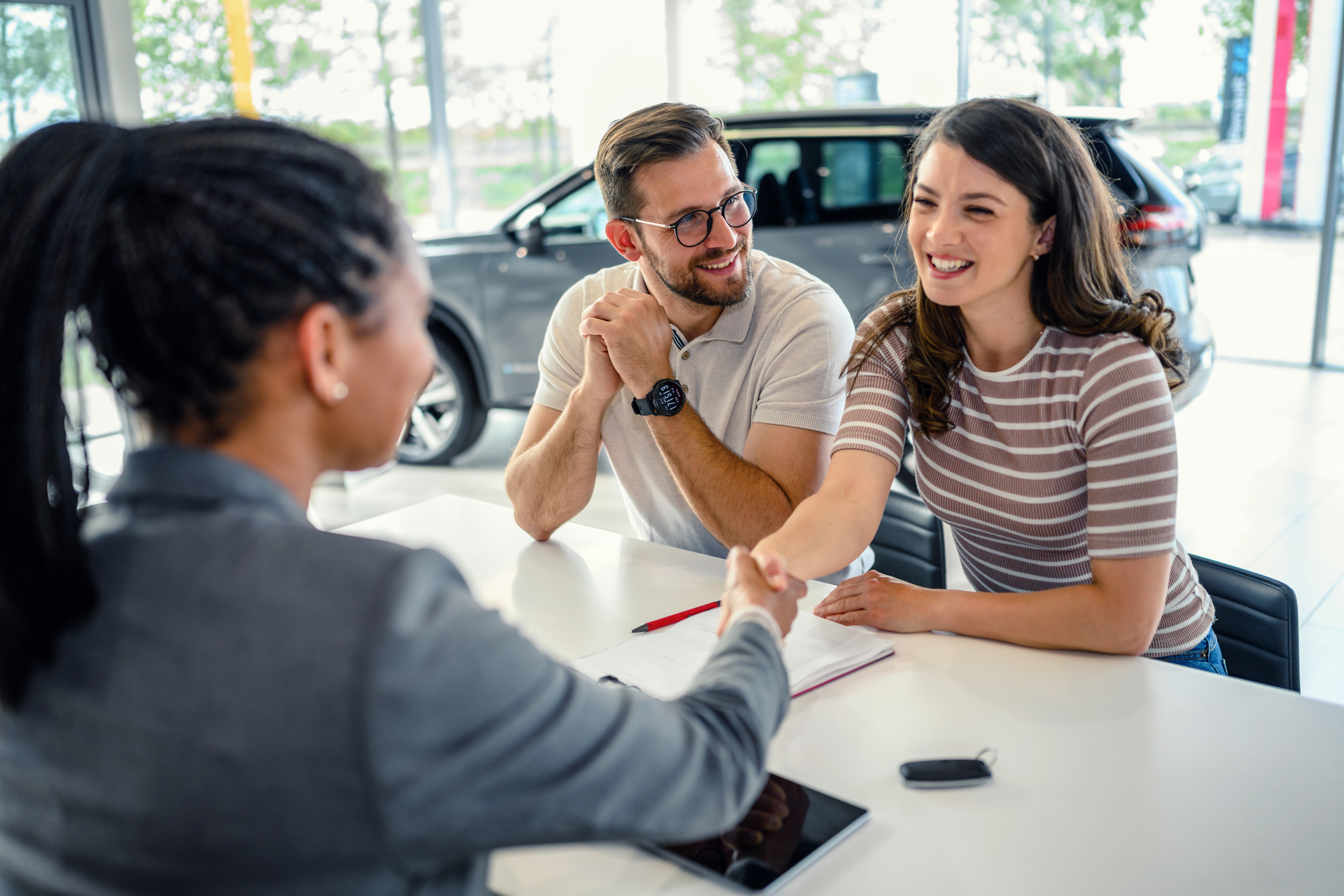 Salesperson shaking hands with a couple buying a car.