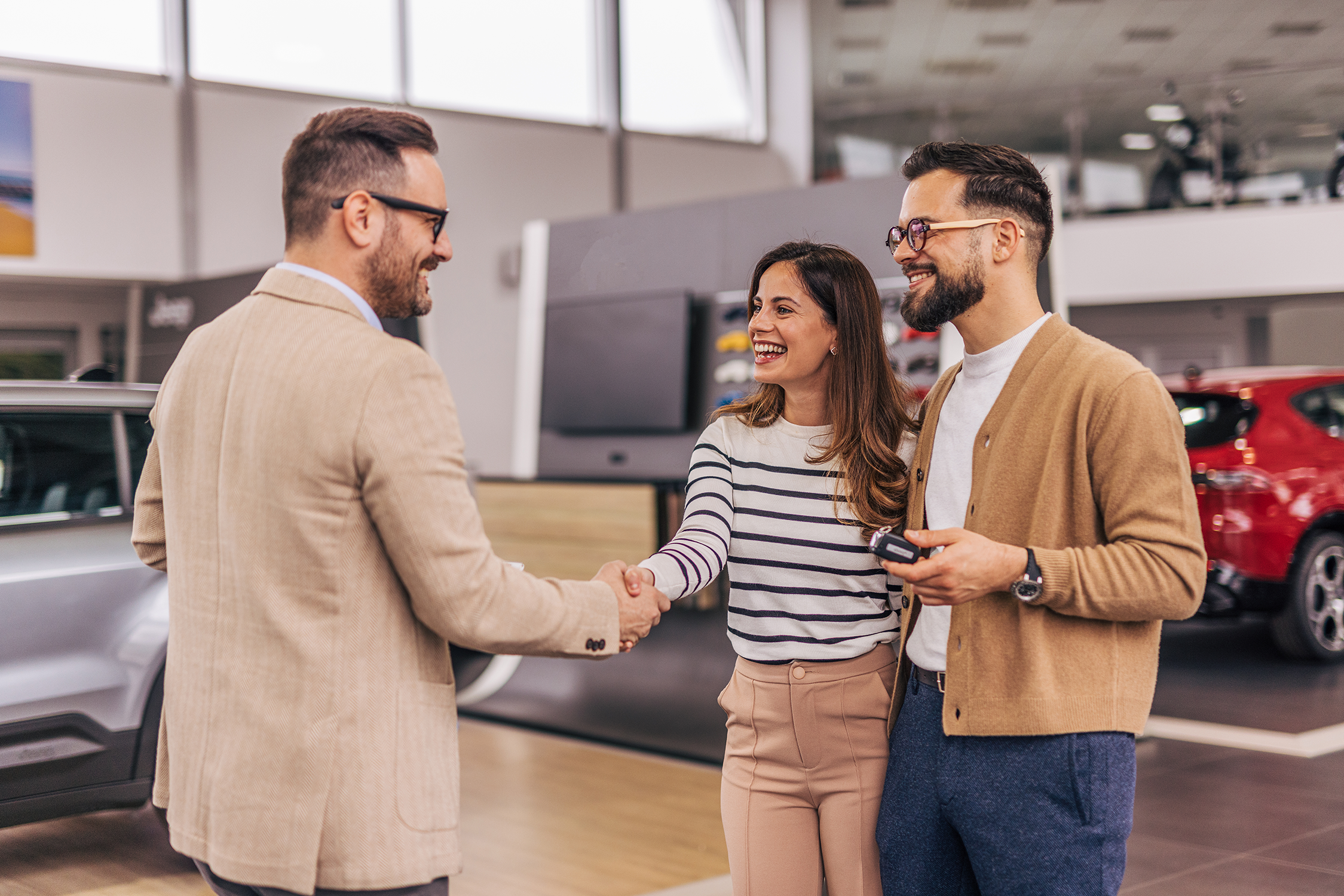 Car salesperson shakes hands with a couple buying a car. 